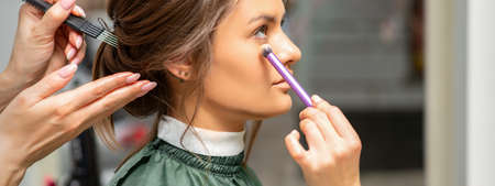 Makeup and hairstyle process. Makeup artist and hairdresser preparing young caucasian woman, working...