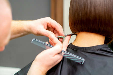 The hairdresser cuts the hair of a brunette woman. Hairstylist is cutting the hair of female client in a professional hair salon, close upの写真素材