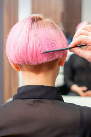 Professional hairdresser brushing short pink hair of young woman with a comb in a hairdressing...