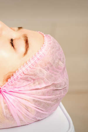 Side view of a young caucasian woman in a medical cap lying with closed eyes waiting for the cosmetic procedure in a beauty salonの写真素材