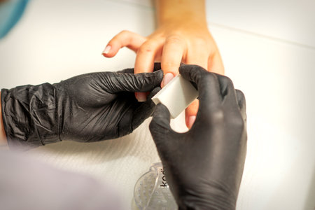 Close up of the caucasian hands of a professional manicurist are filing the nails of a young woman. Young caucasian woman receiving a manicure by a beautician with a nail file in a nail salonの写真素材
