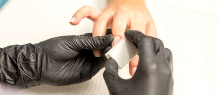 Close up of the caucasian hands of a professional manicurist are filing the nails of a young woman....
