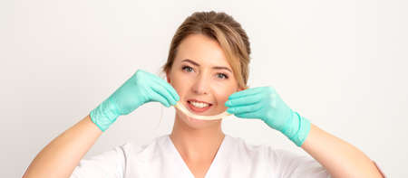 Young caucasian smiling female beautician holding wax for depilation over white background. Yellow...