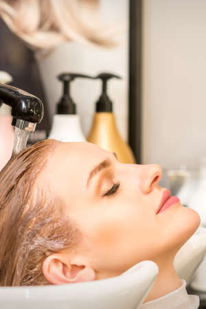 Young caucasian woman with closed eyes getting washing hair by a professional hairdresser in a...