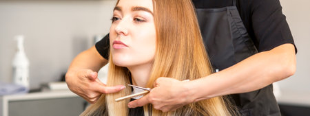 Beautiful young blonde woman with long straight blonde hair getting a haircut at the hairdresser salonの写真素材