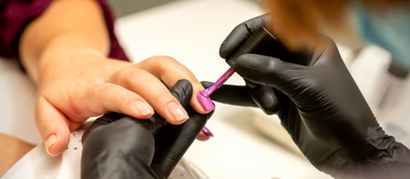 Professional manicure. A manicurist is painting the female nails of a client with purple nail polish in a beauty salon, close up. Beauty industry conceptの写真素材