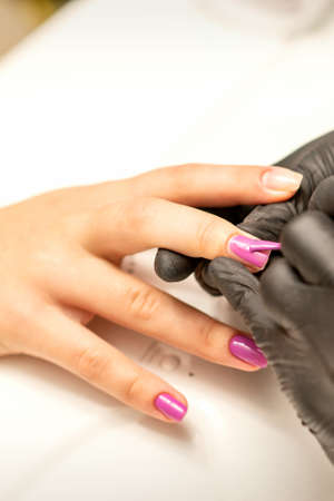 Professional manicure. A manicurist is painting the female nails of a client with purple nail polish...