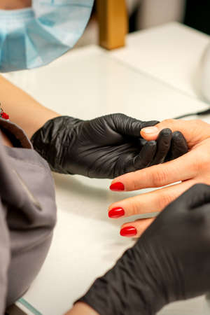Professional manicure. A manicurist is painting the female nails of a client with red nail polish in a beauty salon, close up. Beauty industry conceptの写真素材