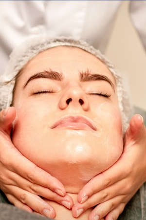 Face massage. Beautiful caucasian young white woman having a facial massage with closed eyes in a...