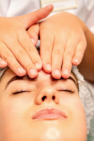 Head massage. Beautiful caucasian young white woman receiving a head and forehead massage with closed eyes in a spa salonの写真素材