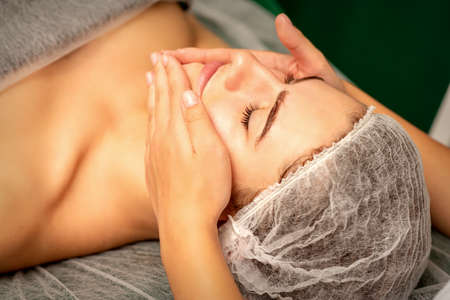 Beautiful caucasian young woman receiving a facial massage with closed eyes in spa salon, close up. Relaxing treatment conceptの写真素材