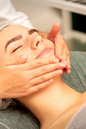 Beautiful caucasian young woman receiving a facial massage with closed eyes in spa salon, close up. Relaxing treatment conceptの写真素材