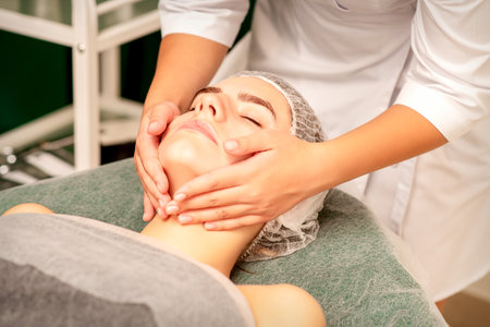 Facial treatment massage. Beautiful young caucasian woman with perfect skin receiving face and neck massage at a beauty spaの写真素材