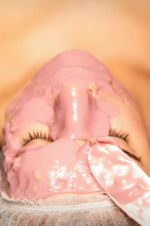 Beautiful young caucasian woman receiving an alginic mask to the face in beauty salon. Facial skin...