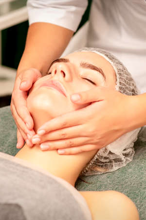 Facial treatment massage. Beautiful young caucasian woman with perfect skin receiving face and neck massage at a beauty spaの写真素材