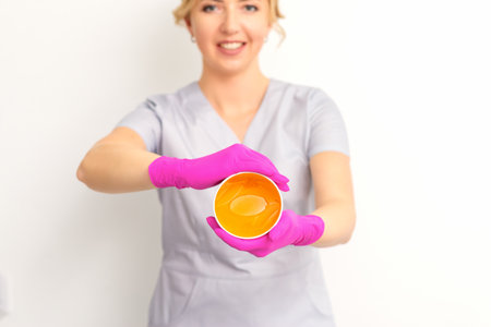 Portrait of a female caucasian beautician holding a jar of sugar paste for sugaring wearing pink gloves on white backgroundの写真素材