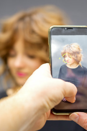 Man hairdresser taking pictures on the smartphone of her clients hairstyle against a gray backgroundの写真素材