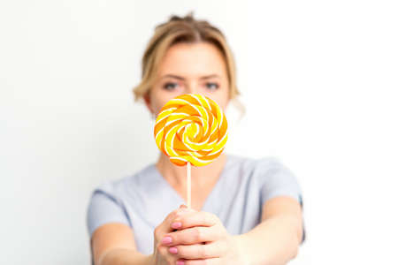 Waxing, depilation concept. The beautician is wearing a medical coat holding a sugar lollipop on...