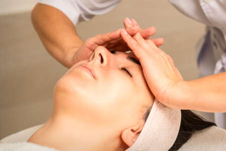 Facial massage. Young caucasian woman with closed eyes getting a massage on her forehead in a beauty salonの写真素材