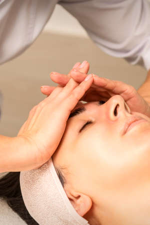 Facial massage. Young caucasian woman with closed eyes getting a massage on her forehead in a beauty...