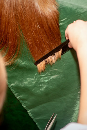 A hairdresser does a haircut and combes the long hair of a brunette woman in a beauty salonの写真素材