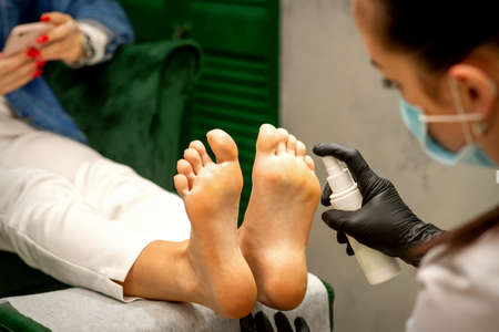 A woman getting a pedicure and pedicurist moisturizing female feet with lotion spraying in a beauty salonの写真素材