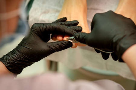 Professional pedicure. Pedicure master wearing latex gloves cuts female toenails in the beauty salon, closeupの写真素材