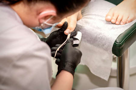 Professional pedicure. Pedicure master wearing latex gloves cuts female toenails in the beauty salon, closeupの写真素材
