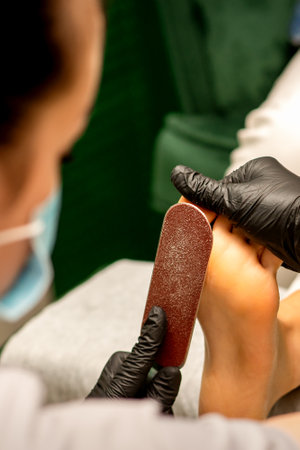 Pedicurist rubbing heel with a special grater on pedicure treatment in a beauty salonの写真素材