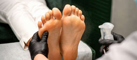 A woman getting a pedicure and pedicurist moisturizing female feet with lotion spraying in a beauty...