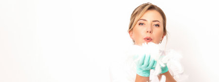 Young beautiful woman beautician in protective green gloves standing and blowing on feathers over...