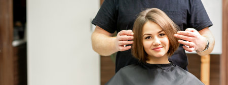 Gorgeous brunette short hair woman and her male hairdresser looking and checking out hairstyle. Beautiful hairstyle of a young brunette woman, results of hair treatment in a beauty salonの写真素材