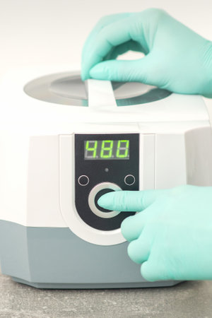 Beautician in protective gloves starts the machine for disinfection of tools before the medical procedureの写真素材