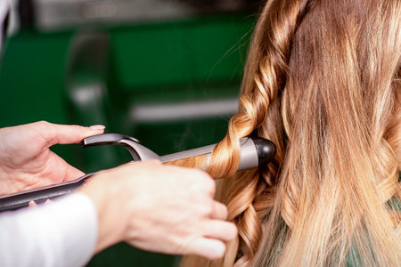 The female hairdresser is curling hair for a brown-haired young caucasian woman in a beauty salonの写真素材