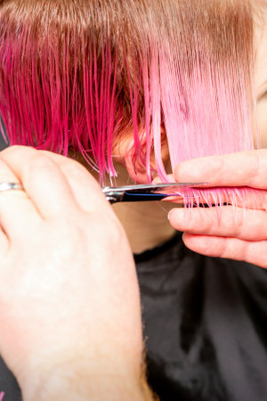 Haircut of dyed short pink wet hair of young caucasian woman by a male hairdresser in a barbershopの写真素材