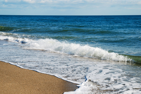 Waves of the blue sea surge in sand shore  White foam glows between sandy coast and turquoise water surface reflecting azure sky  There is nobody の写真素材