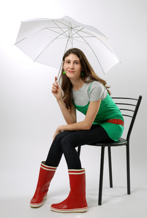 Teenage girl is sitting on the chair  She is holding an umbrella  She is wearing the red boots and green dress  の写真素材