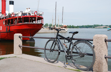 The city bike is parked to railing of jetty in the gulf of Helsinki  People rest in the big red ship converted for a cafe のeditorial素材
