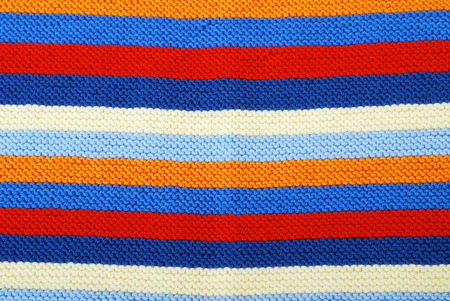 Multicolored fabric is knitted by hand  It has horizontal pattern composed of red, white, blue,...