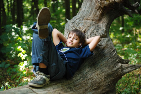 Teenage boy is lying on trunk and listening to music  Gadget is on his chest  Small earphones is in...