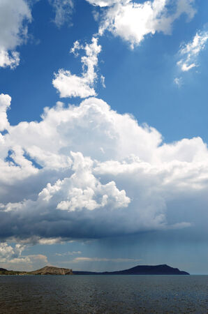 Huge cumulus cloud is raining the darkened sea  There is remote cape between the sky and the sea の写真素材
