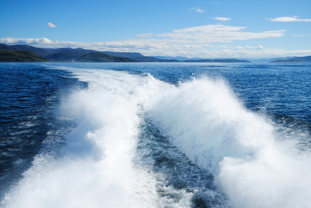 Powerful foam trace of hovercraft is receding into the distance  There are blue fjord, dark cliffs and the north sky の写真素材