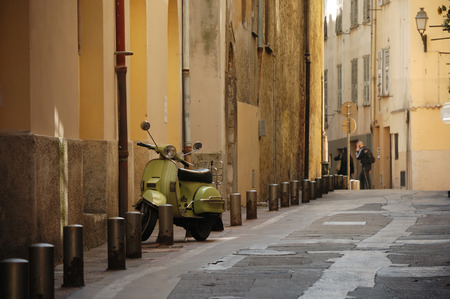 Empty old street with special columns along and green motorcycle parked, fawn-coloured walls of old housesの写真素材