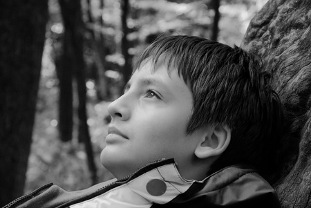Profile of the pensive teenage boy is photographed close-up outdoors  He is looking upwards  He is lying on the tree の写真素材