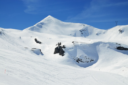 A lot of ski runs on the snowy downhills against the blue sky and a peak in the winter Pyrenees.