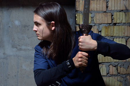 A serious teenage boy is stealing along the wall of the abandoned building. He holds the sword.の写真素材