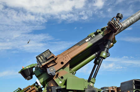 The modern antiaircraft gun is photographed against the sky with a military helicopter.