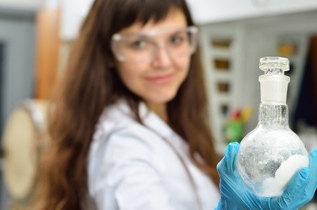 A young researcher holds a flask with a substance in the chemical laboratory. She is wearing an...