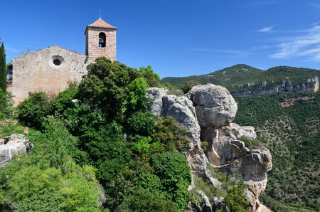 The ancient church is extant on the steep slope overgrown with lush verdure in the Prades Mountains.の写真素材