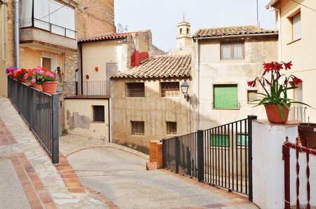The steep street of the overhanging houses is decorated with flowers, rails and floor tiles in the old part of the Spanish town El Pinell de Brai.の写真素材